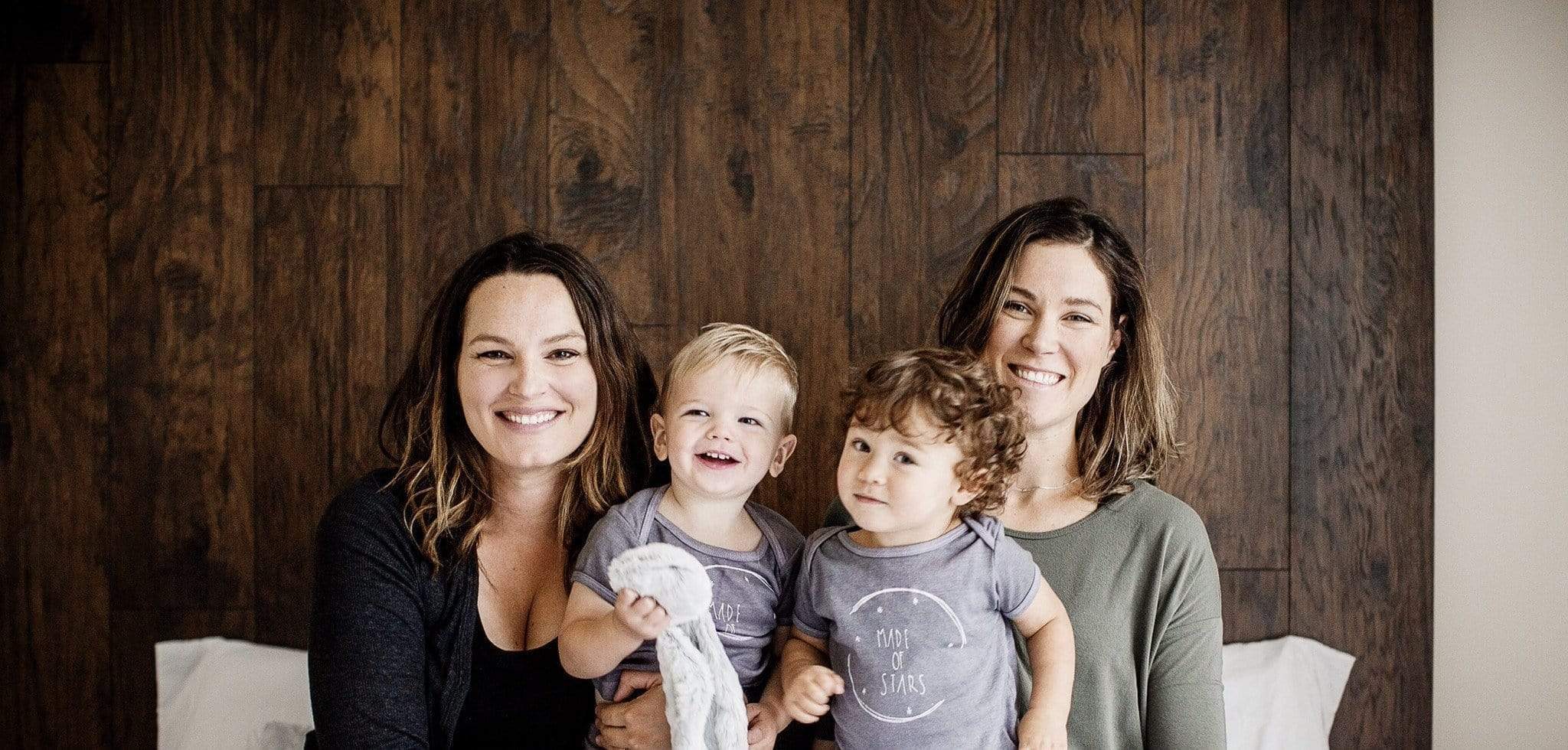 Two adults pose with two young children in front of a wooden wall