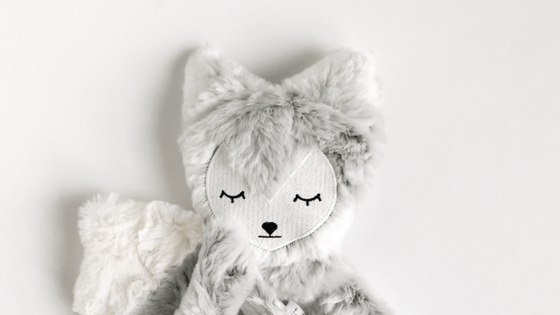 Close-up front view of gray fox plush with embroidered closed eyes and soft faux-fur texture on a light background