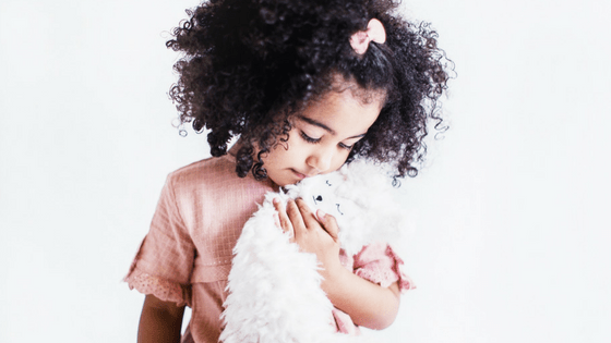 Young girl hugging a white fluffy stuffed animal against a bright white background