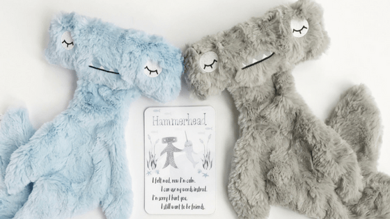 Flat-lay of two Hammerhead plush toys with soft blue and gray fur, embroidered sleepy faces, white background and story card