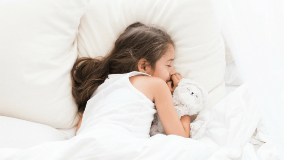 Young girl sleeping on a white bed hugging a stuffed lamb in a cozy bedtime setting