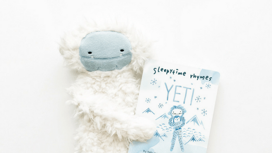 Front view of Yeti plush holding a Yeti storybook showcasing soft white fur and a smiling embroidered face on a white background