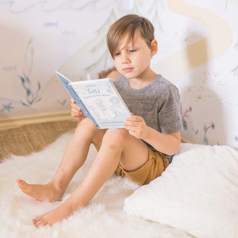 Child reading a book in a cozy comfort corner on a fluffy white rug with a soft pillow and muraled wall