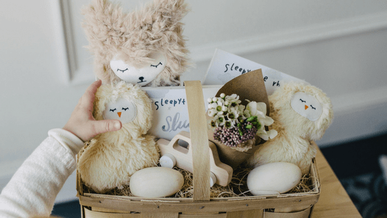 Easter basket filled with plush toys, a wooden toy, flowers, and white eggs on a table