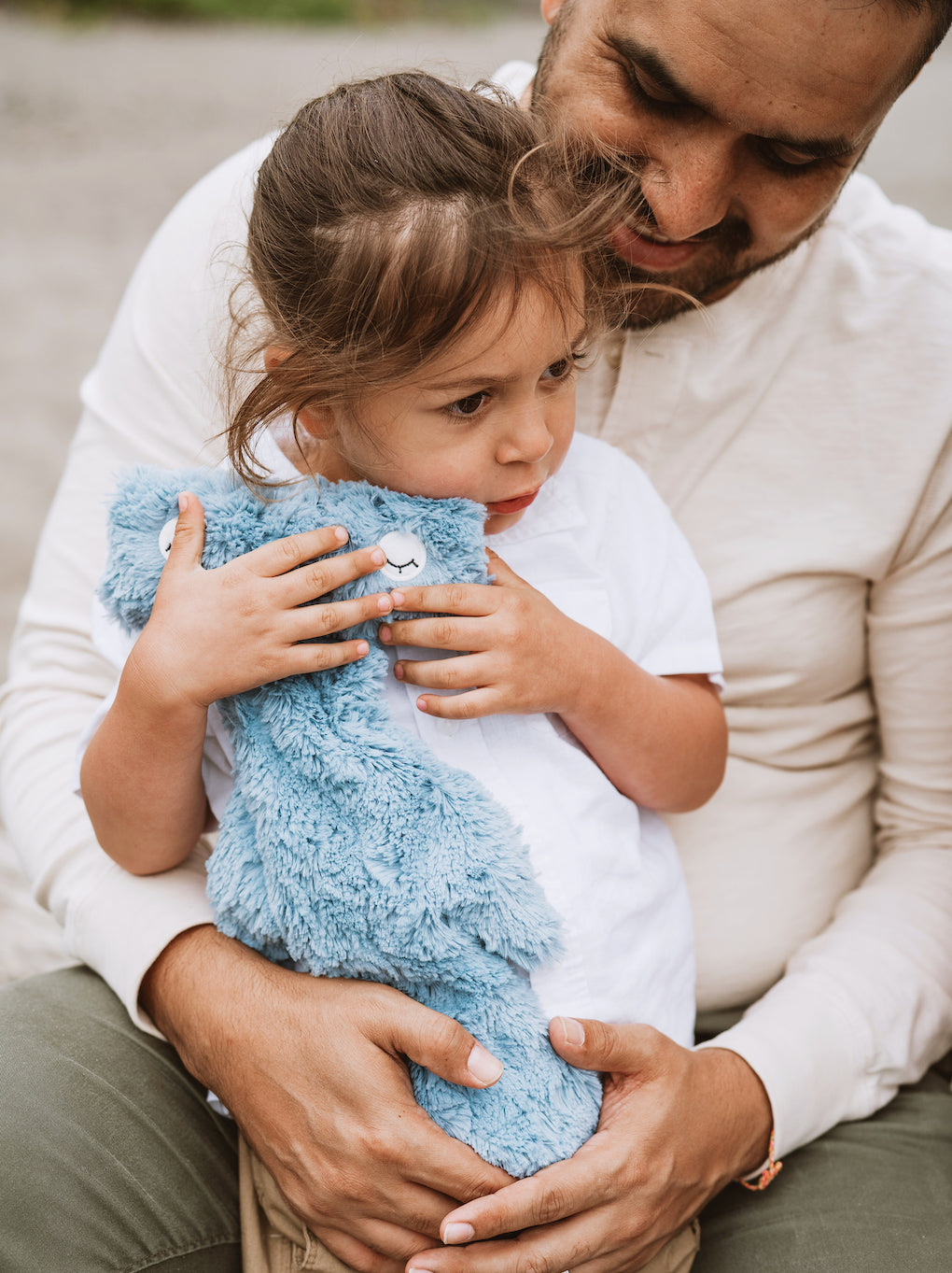 Father comforting a toddler holding a blue plush blanket while sitting on his lap outdoors