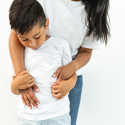 Woman hugging a young boy from behind, comforting him against a plain white background