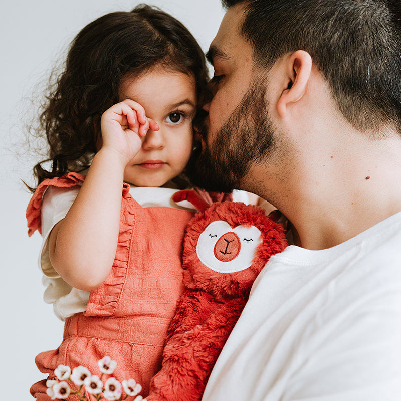 Caregiver kissing child holding a red plush toy in a comforting moment