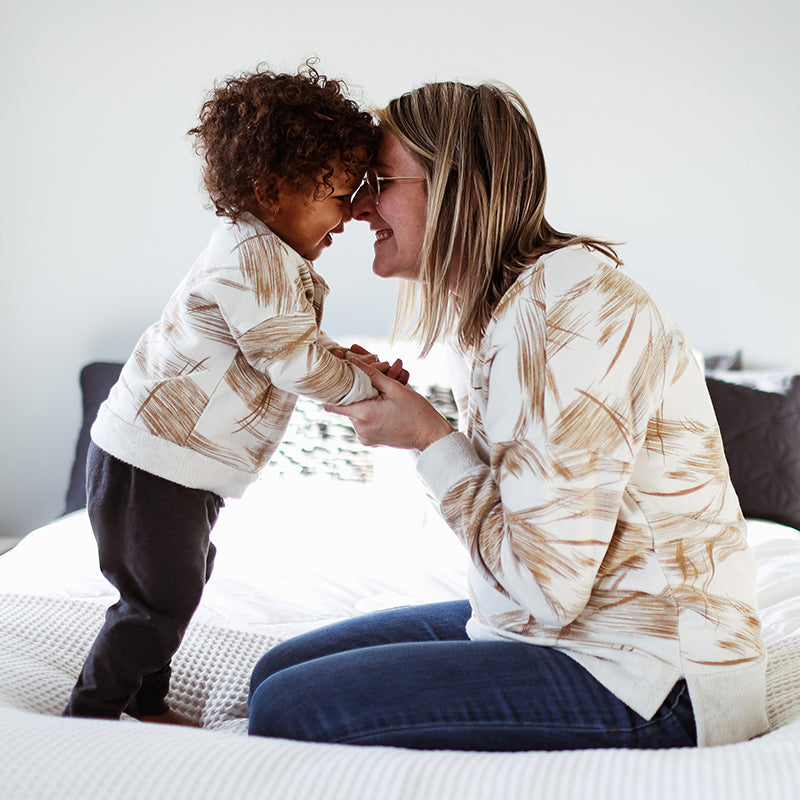 Caregiver and toddler touch foreheads and hold hands on a bed, smiling