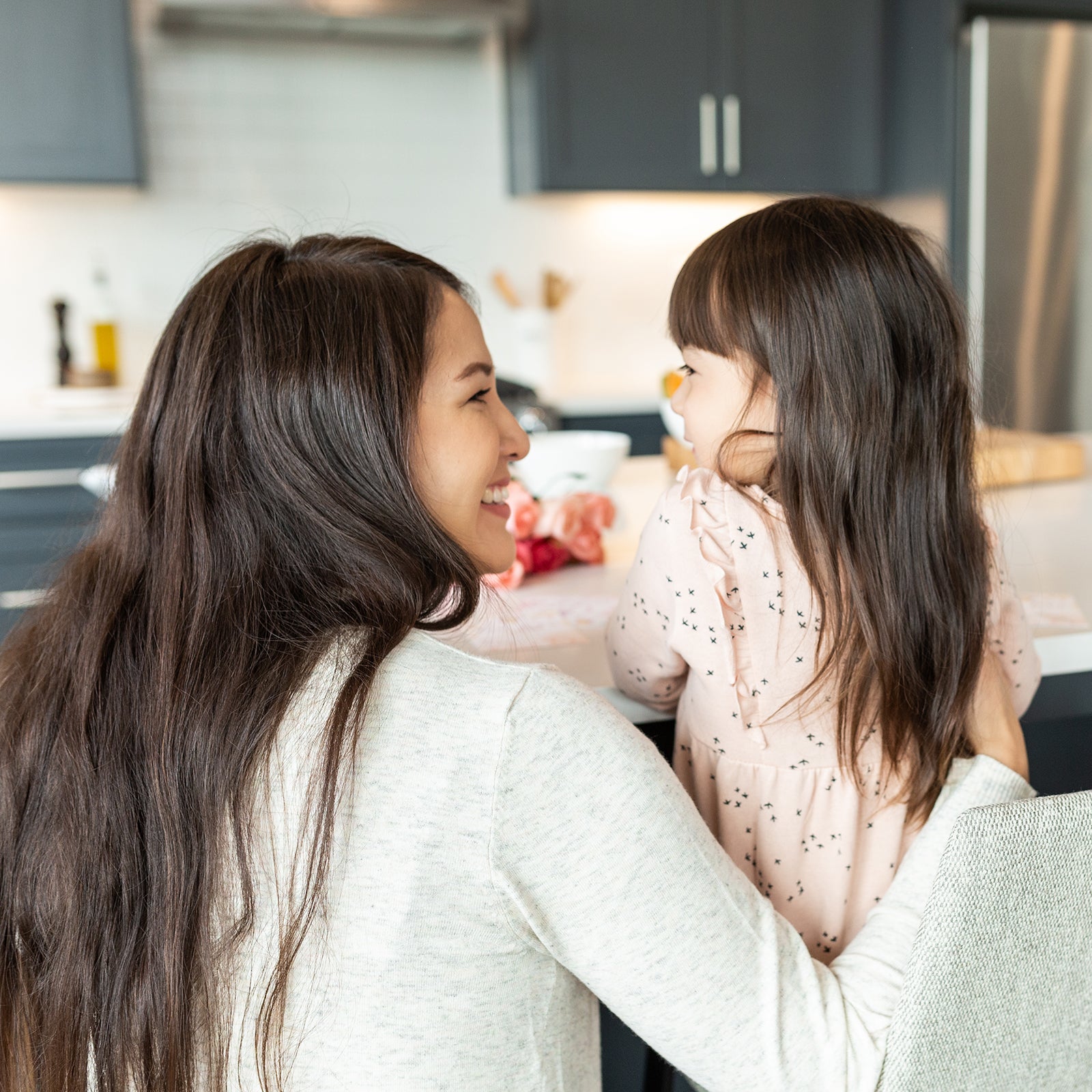 Mother smiling at her young daughter at a kitchen counter, sharing a tender moment