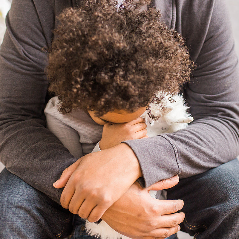 Child being comforted by an adult in a close embrace while holding a white plush toy