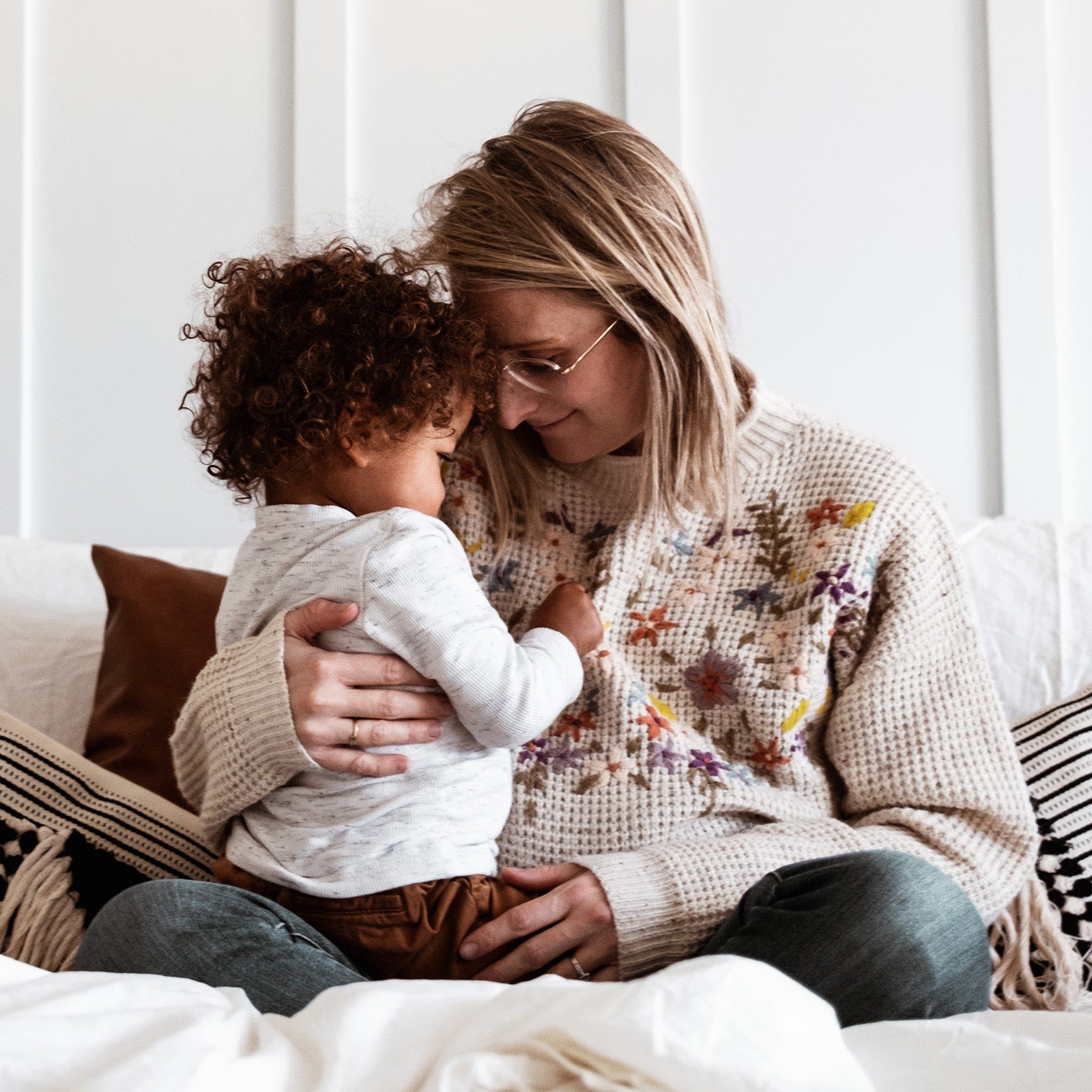 Woman holding and comforting a toddler on a couch in a softly lit room