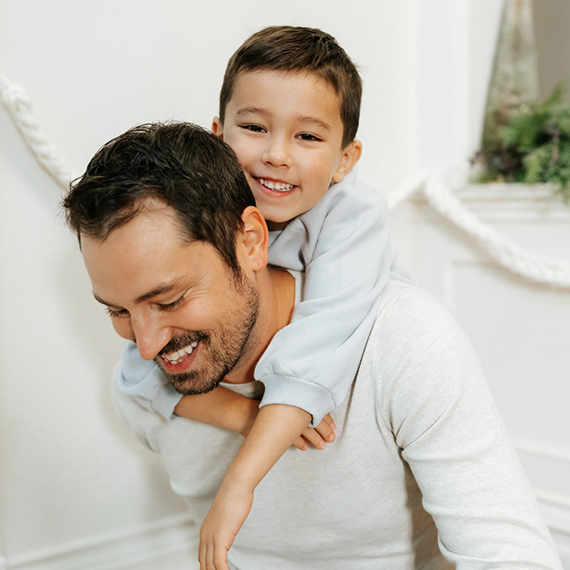 Smiling father giving a piggyback ride to his young son in a bright, cozy home setting