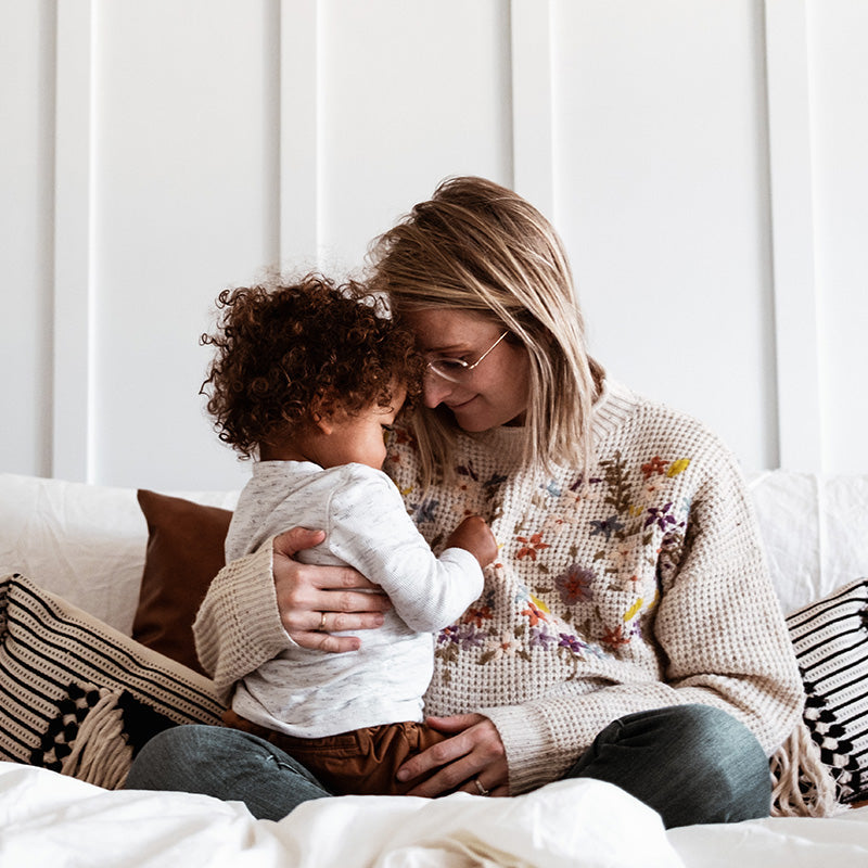 Caregiver holding a toddler and sharing a quiet comforting moment on a bed with striped pillows