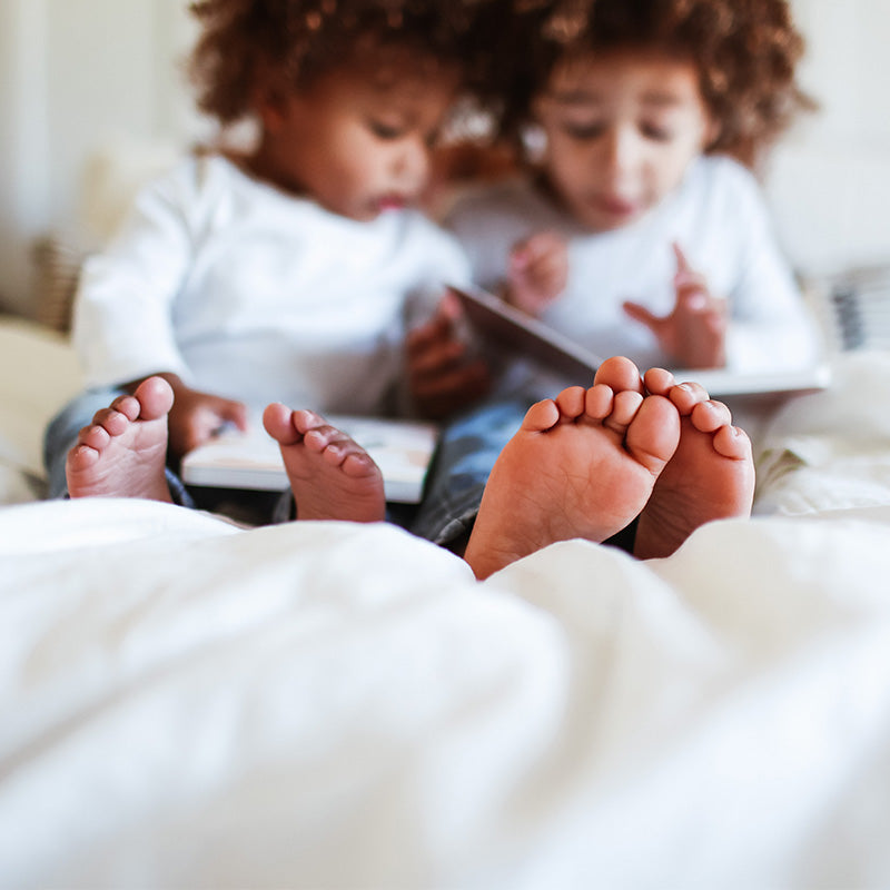Two children sharing a tablet while sitting on a bed, close-up of their bare feet in the foreground