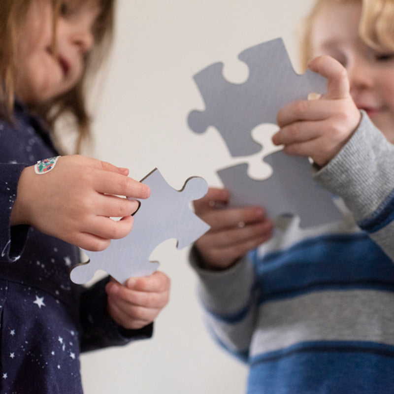 Two children holding large puzzle pieces together in a close-up, focusing on their hands and the pieces