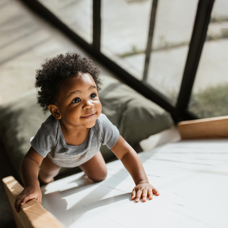 Toddler crawling and smiling on a white surface near a sunlit window