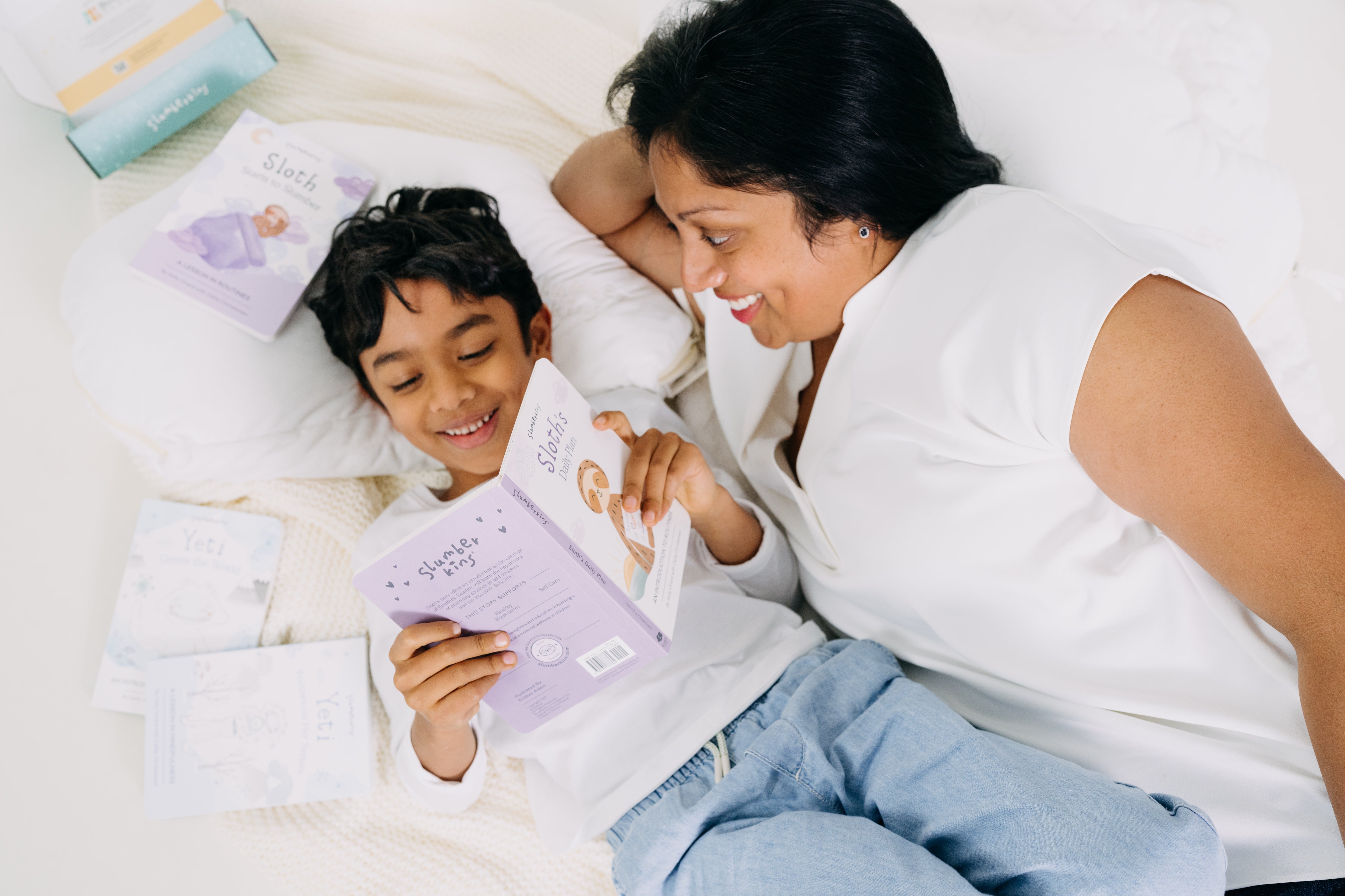 Mother and son reading a Slumberkins book together on a bed, both smiling