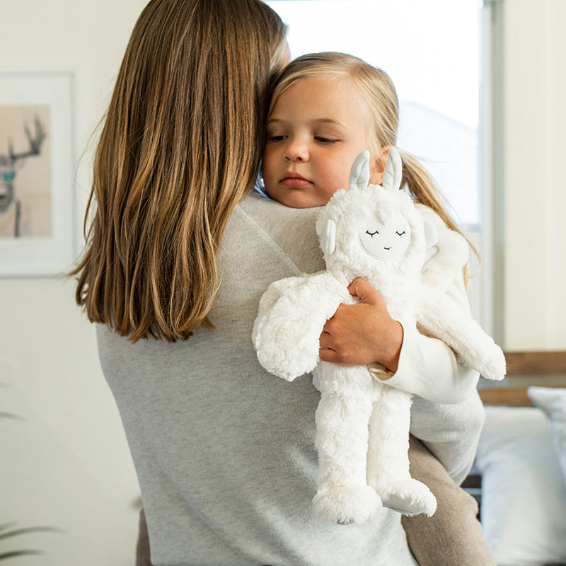 Young child being comforted by a caregiver while holding a white plush comfort toy in a softly lit bedroom