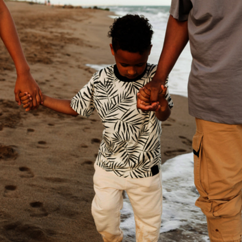Young child walking on a sandy beach holding hands with two adults, waves at the shoreline