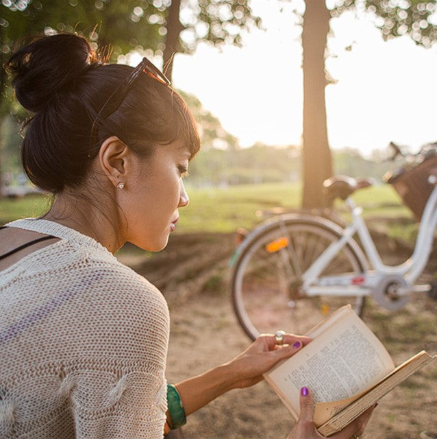 Woman reading a book outdoors at sunset with a parked bicycle in the background