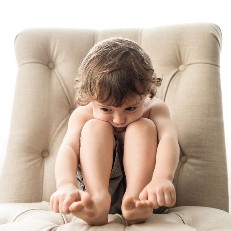 Young child curled up on a beige tufted armchair looking thoughtful and bored