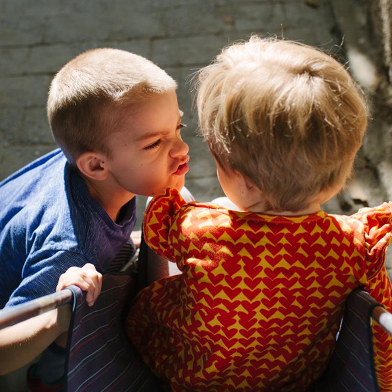 Two young children on a playground, one leaning forward and scowling at the other