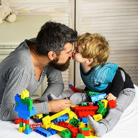 Father and young son kiss while playing with colorful building blocks on a bed, headline ‘5 Types of Play for Child Development’