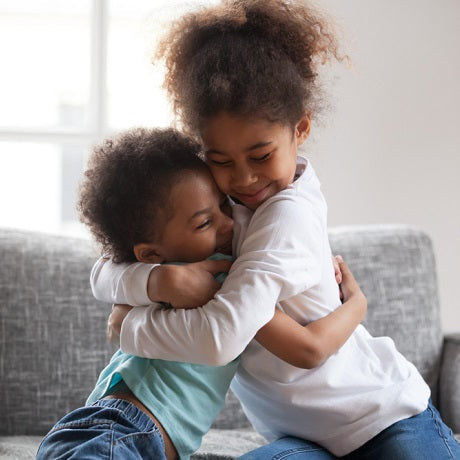 Two children hugging on a gray couch, smiling and showing affection