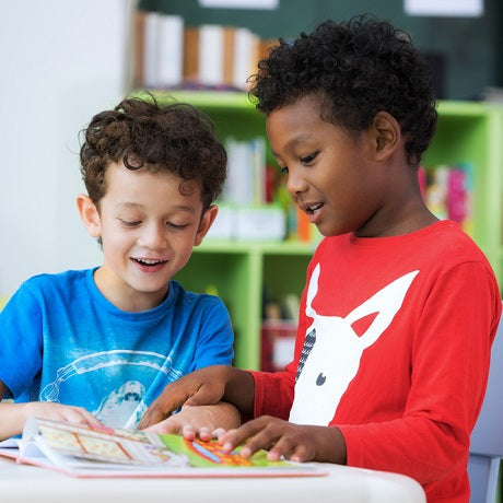 Two children reading a book together at a classroom table