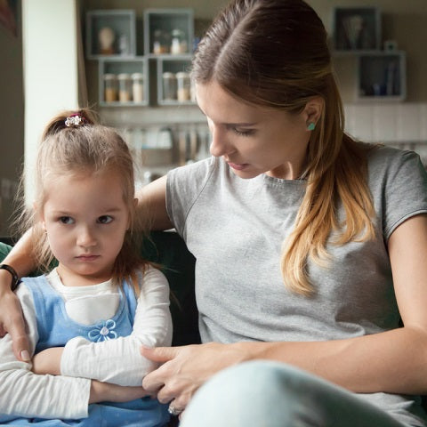 Adult comforting a young girl sitting on a couch in a living room, modeling calming support