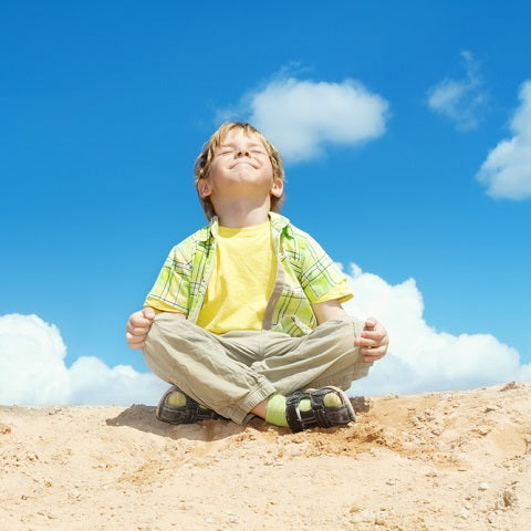 Boy sitting cross-legged meditating on a sunny sandy hill under a bright blue sky