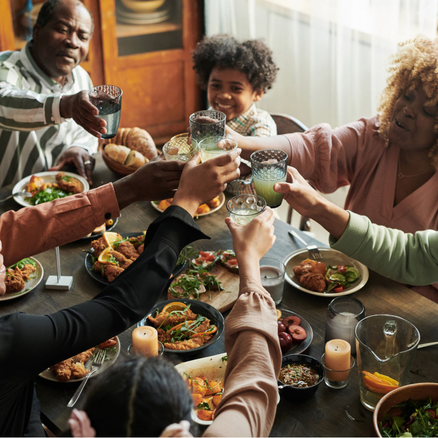 Family raising glasses in a warm holiday dinner toast around a table of shared dishes