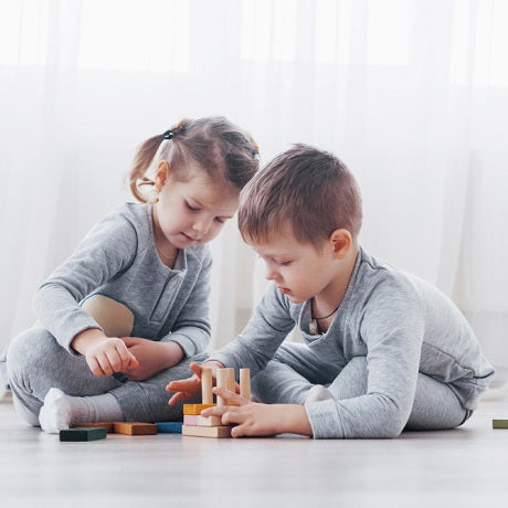 Two children playing with wooden blocks on the floor in a bright room