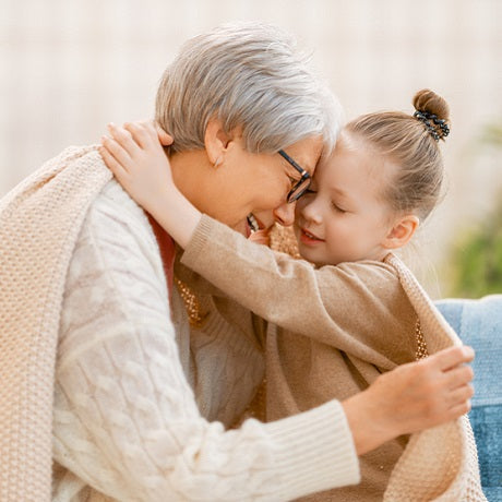Woman hugging a young girl on a couch, both smiling in a cozy living room