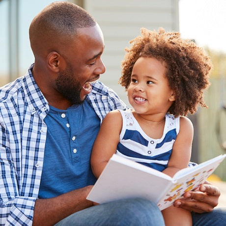 Father reading a picture book to his smiling young daughter outdoors