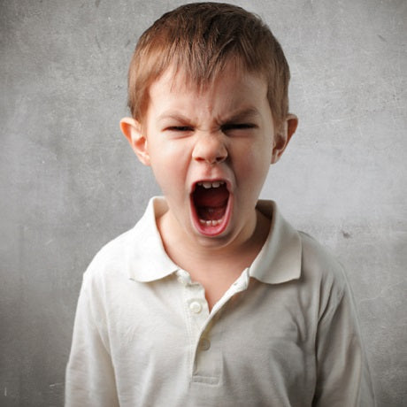 Angry young boy yelling with his mouth wide open against a textured gray background