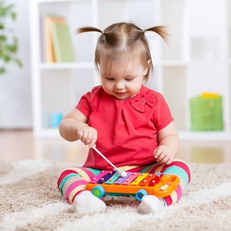 Toddler sitting on a carpet playing a colorful xylophone toy in a bright playroom