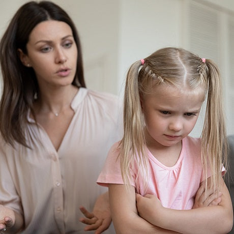 Mother talking to an upset young girl with crossed arms in a home setting, child refusing to respond