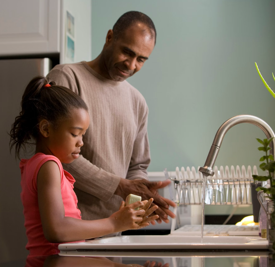 Father helping his young daughter wash hands at a kitchen sink in a calm home setting