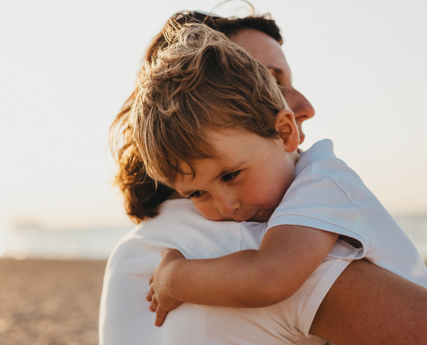 Young boy being hugged by an adult on a beach at sunset