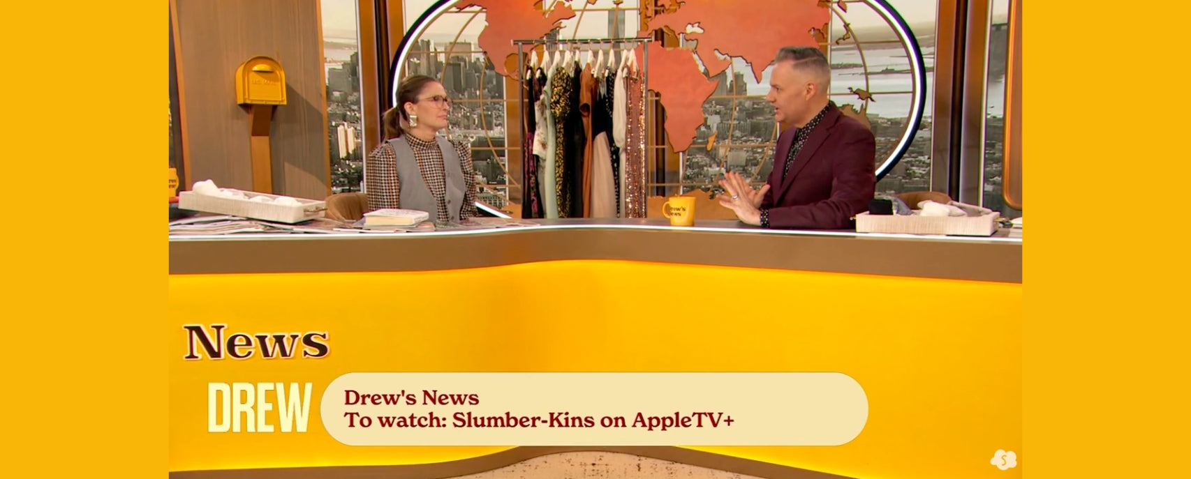 Screenshot showing Drew’s News segment with headline “To watch: Slumber-Kins on AppleTV+” and two hosts seated at a studio desk