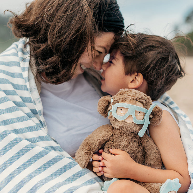 Caregiver and child wrapped up on beach with Bigfoot Kin