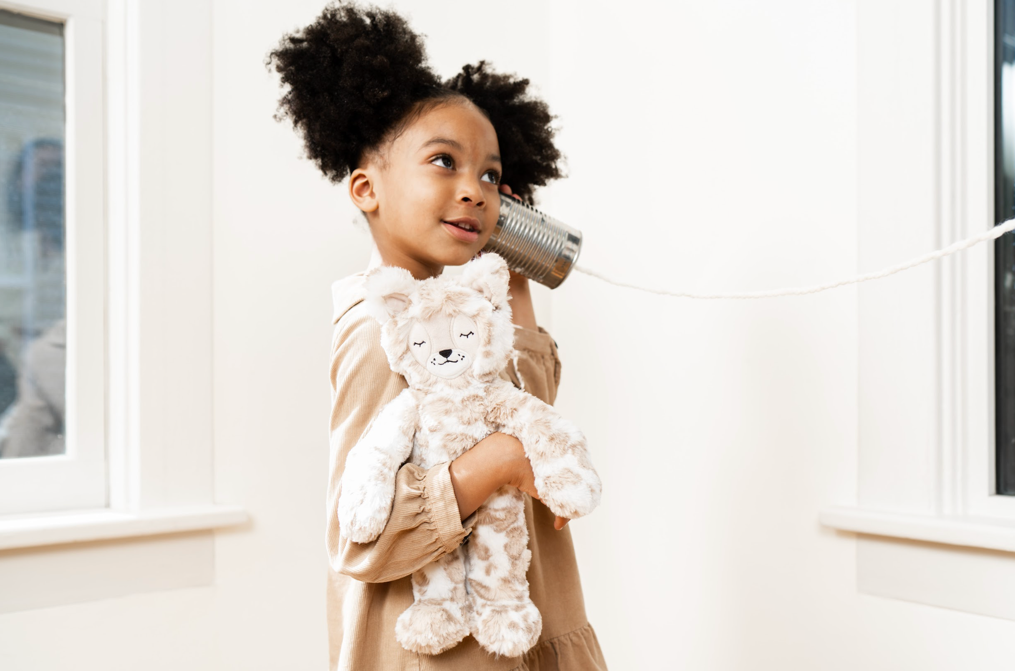 A young girl showing how to overcome shyness while holding a stuffed lynx and listening to something through a tin can and string