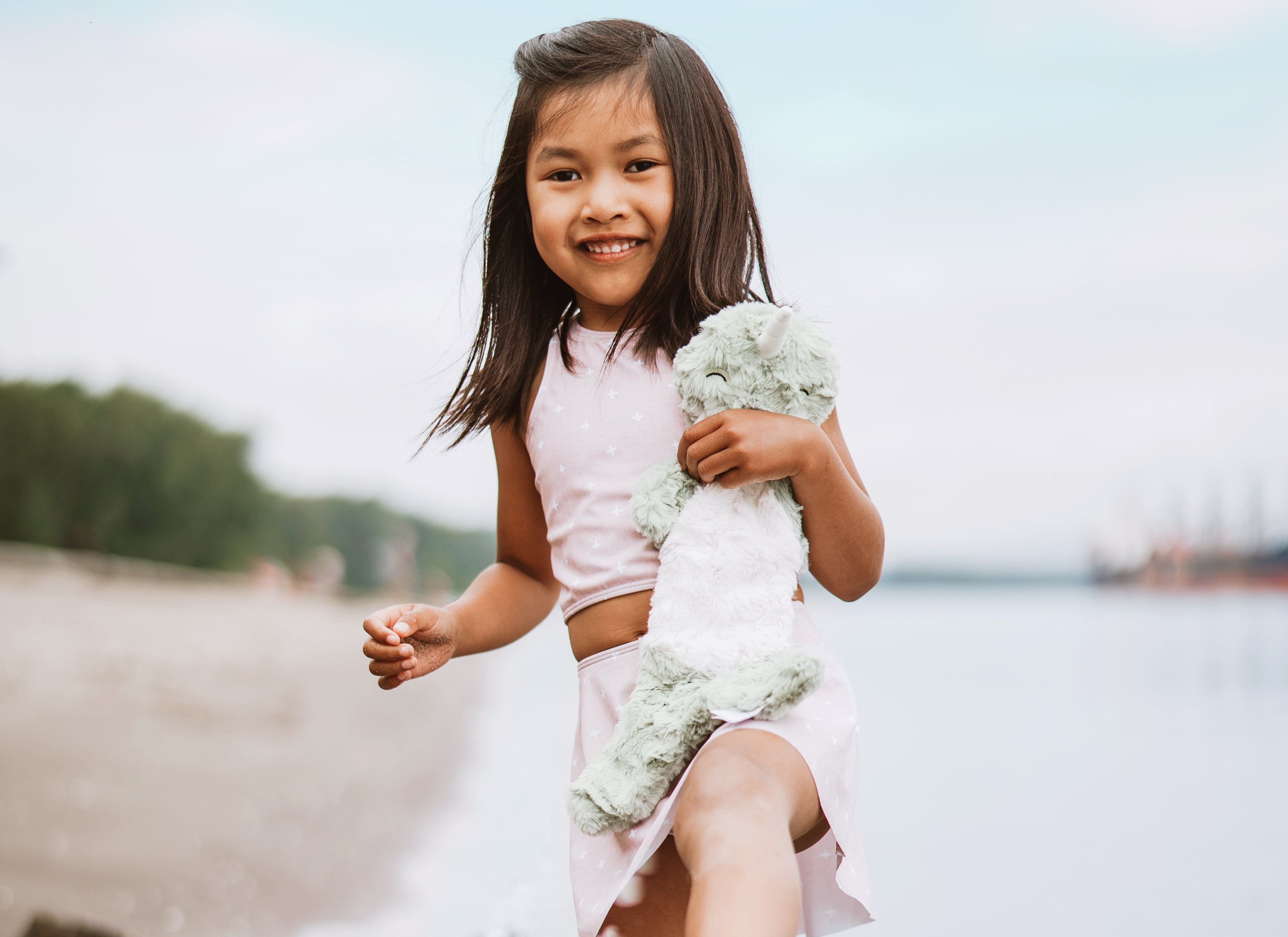 A young girl splashes in a lake with her Slumberkins stuffed animal in her hands