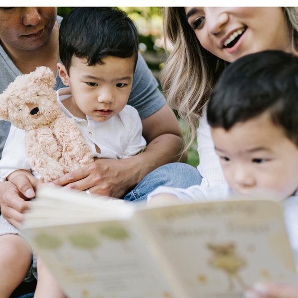 Caregivers reading Honey Bear's board book to two children while one holds Honey Bear Kin