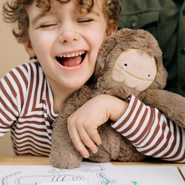 A child smiling big while he hugs his Bigfoot Kin!