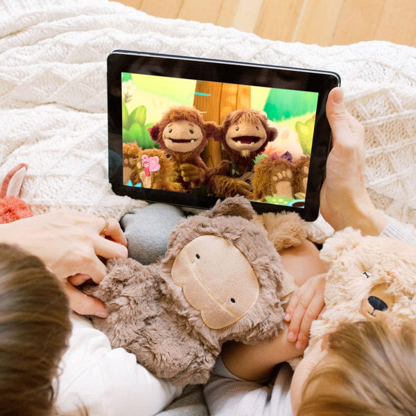 Two children holding a Bigfoot and Honey Bear Snuggler while watching Slumberkins on AppleTV+